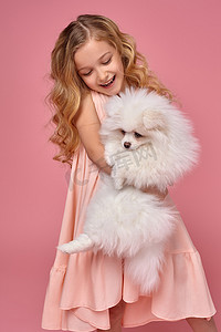 一头金发卷发、穿着粉色裙子的小女孩和她的狗玩耍