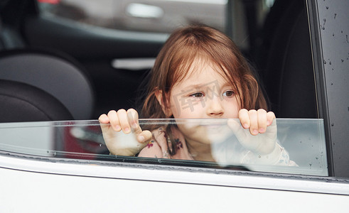 可爱的小女孩透过窗户看车。