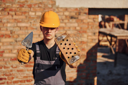 建筑工人穿着制服和安全设备站在建筑物上拿着砖块和工具的画像