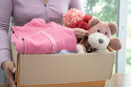 在家里拿着装有旧衣服和洋娃娃的衣物捐赠箱，支持帮助世界上的穷人。