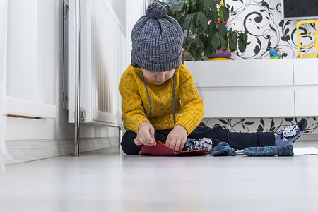一个穿着黄色毛衣和帽子的小男孩正在数钱和研究取暖费，旁边是一个带恒温器的加热器。