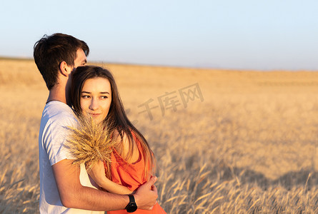 拥抱他的女朋友的年轻人在麦田的日落。