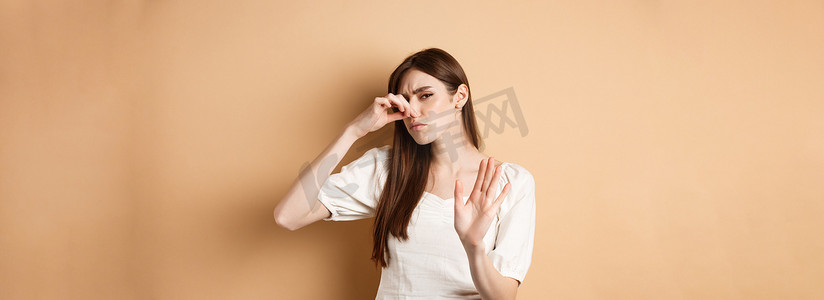 厌恶摄影照片_不高兴的女人从难闻的气味中塞住鼻子，表现出停止的姿态，厌恶地皱着眉头。