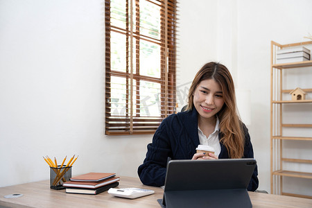 财务办公摄影照片_亚洲女性使用笔记本电脑，在办公室工作，在办公桌上使用计算器文档，进行规划分析财务报告、商业计划投资、财务分析概念。