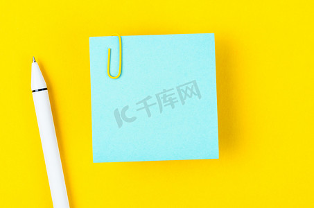 一张空白的蓝色笔记纸和一支笔，黄色背景上有一个回形针，用于您的文本或消息。