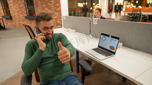 在现代联合办公空间的办公桌前，留着胡子的白种人用智能手机聊天。