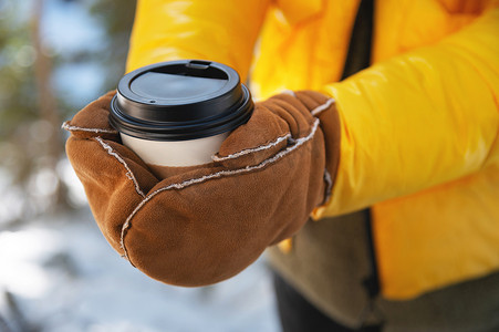 戴着手套的女人在户外公园的冬季城市里拿着纸杯咖啡。