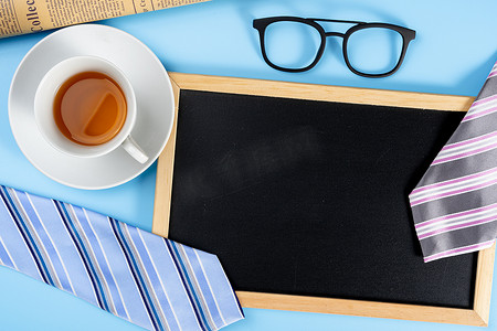 父亲节快乐背景概念，蓝色和粉色领带眼镜、报纸、茶杯和蓝色背景的黑板，带有文本复制空间。