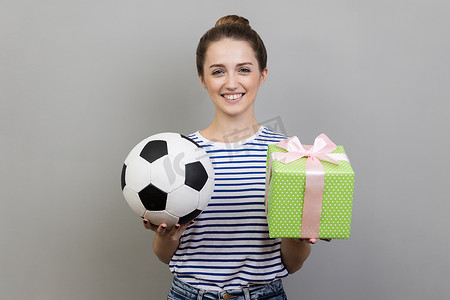 女人站着看着镜头微笑，拿出足球和礼物盒。