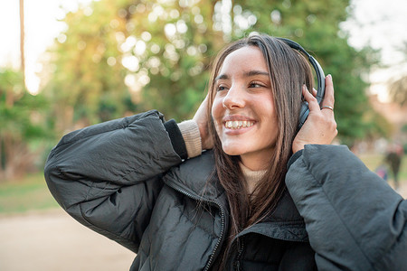 快乐的女人戴着耳机享受音乐，在公园的户外播客我们的有声读物。