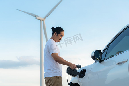 汽车作为摄影照片_有他的 EV 汽车和风力涡轮机作为可再生能源概念的进步人。