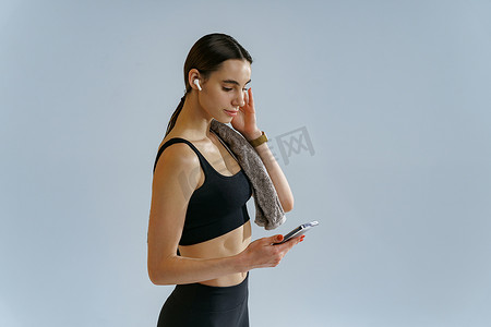 健身美女戴耳机摄影照片_在工作室背景下训练和听音乐后戴耳机的美女