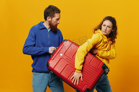 女人和男人微笑着，手里拿着手提箱，黄色和红色的手提箱愉快地微笑着，弯曲着，黄色背景，去旅行，家庭度假旅行，新婚夫妇。
