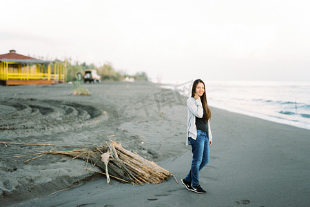 黑山波德戈里察 — 27 08 2022：微笑的年轻女子站在海滩上，靠近一堆干芦苇