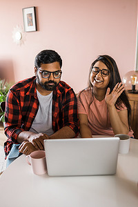 拉丁裔或印度男女夫妇在客厅里使用笔记本电脑进行视频通话。
