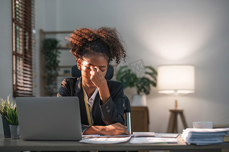 留着爆炸式发型的年轻非洲裔美国女性看起来既恼火又压力重重，坐在办公桌前，用笔记本电脑思考并看着镜头，感到疲倦和厌倦抑郁症