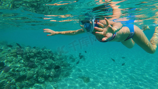 在海里，一个戴着特殊浮潜面具的女孩在炎热的夏日度假时游泳、检查鱼群、围栏和海底世界的美景。