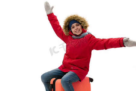 穿着温暖冬装的微笑少年旅行男孩，坐在手提箱上，出国旅行，周末度假