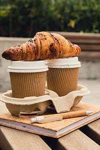 两个带盖的纸杯上放着新鲜出炉的巧克力羊角面包，可以用来盛茶。