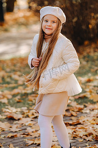 一个戴着帽子的快乐女孩在秋天的公园里散步