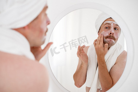 男人在刮胡子后用须后水霜照镜子摸脸