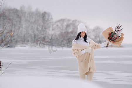 一个穿着米色开衫和冬花的女孩在下雪的季节在大自然中漫步。