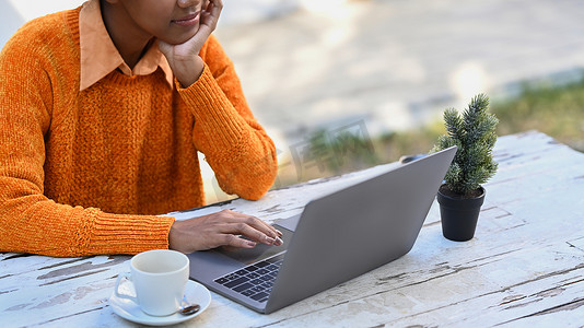 非洲年轻女性在户外咖啡馆放松并在木桌上使用笔记本电脑的剪影