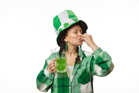 戴着带三叶草叶子的派对帽的快乐女人，做美味的手势，享受圣帕特里克节绿色啤酒的味道