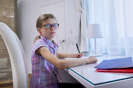 女童坐在家里靠近窗边的办公桌前，在笔记本上写字