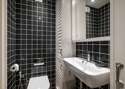 漂亮的浴室配有黑色光滑的方形瓷砖、带水龙头的白色陶瓷水槽和木制毛巾储物柜。