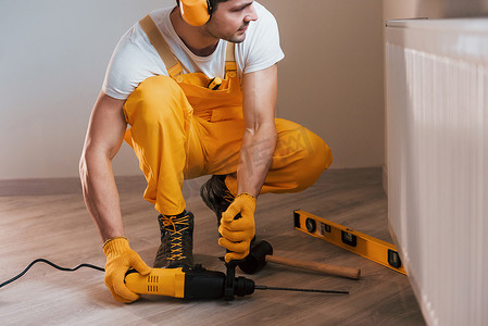 家杂摄影照片_穿着黄色制服的杂工在室内使用锤钻工作。