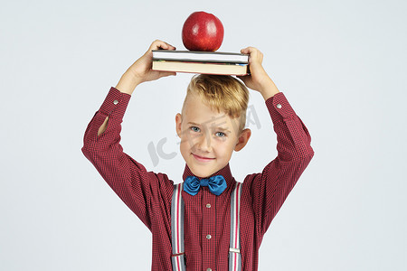 一个小学生拿着书，头上顶着一个苹果，微笑着。