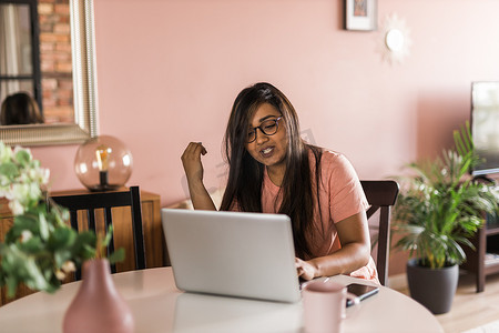 拉丁裔或印度裔女性在客厅使用笔记本电脑进行视频通话。