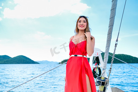 白天乘船游览时，穿着红色裙子的漂亮亚洲女人站在游艇的船头。