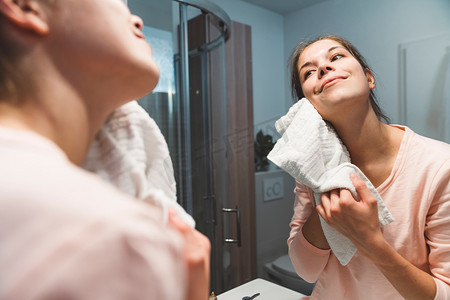 女人一边用毛巾轻轻地擦脸，一边看着浴室的镜子