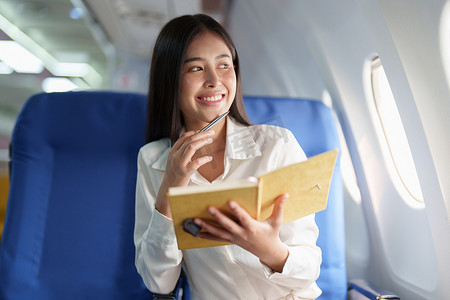 豪华飞机摄影照片_亚洲商务女性乘客坐在商务舱豪华飞机上，同时使用笔记本书工作，同时旅行概念