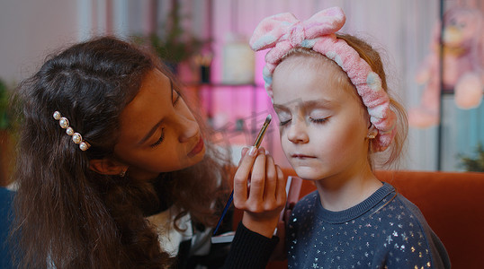 十几岁的孩子在家里的游戏室里帮她的小妹妹做面部化妆
