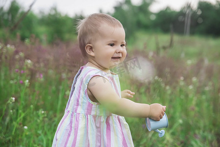 穿着条纹裙子的漂亮婴儿在花园里浇花