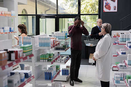 头痛的非洲裔美国顾客向药房高级药店工作人员索取偏头痛药
