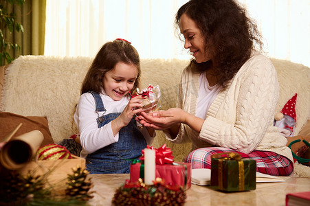 小女孩享受快乐的寒假，帮助她的母亲在舒适的家庭室内包装圣诞礼物