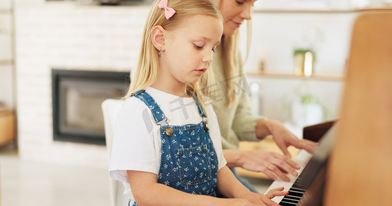 音符字幕框摄影照片_音乐发展、女孩在家里客厅里从妈妈那里学习钢琴和音符教育。
