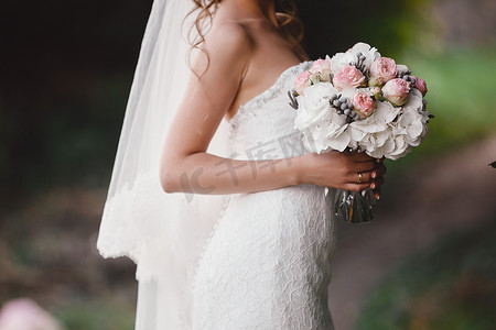 穿着优雅婚纱的新娘手捧一束由不同花朵和绿叶组成的美丽花束。