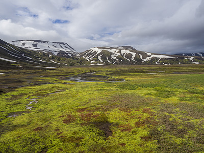 在冰岛自然保护区 Fjallabaki 的 f210 路附近的地热区，夏季景观与五颜六色的绿色和橙色苔藓草甸与温泉和积雪覆盖的流纹岩山脉