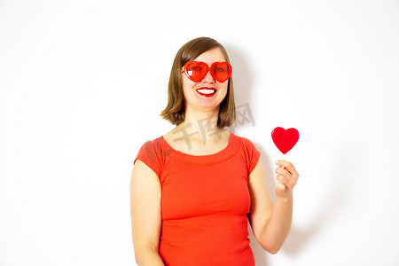 美丽的年轻女子在白色背景上的红色心形太阳镜与一个红色的心形棒棒糖。