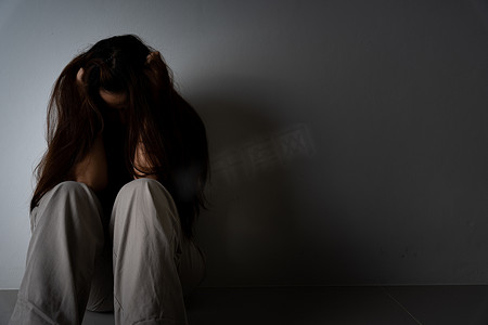 悲伤的女人抱着她的膝盖，独自坐在黑暗的房间里哭泣。