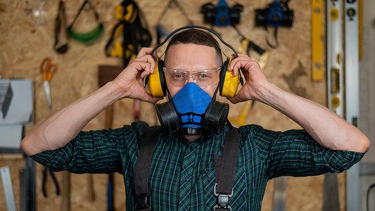 戴着护目镜和呼吸器的木匠戴上隔音耳罩。
