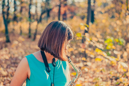 金色裙子摄影照片_身穿蓝色裙子的黑发女人在黄色的秋季公园里吹萨克斯管