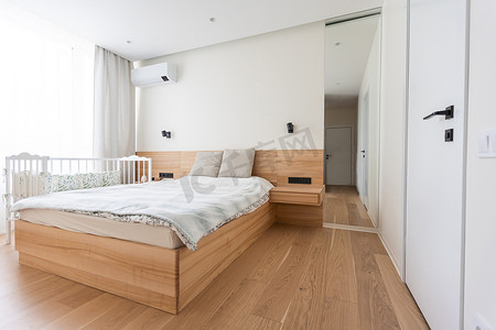 明亮舒适的现代卧室内部配有婴儿床、白色墙壁和镶木地板。