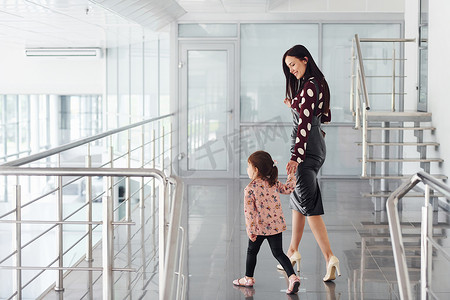 年轻的母亲带着女儿在办公室或机场在室内散步。
