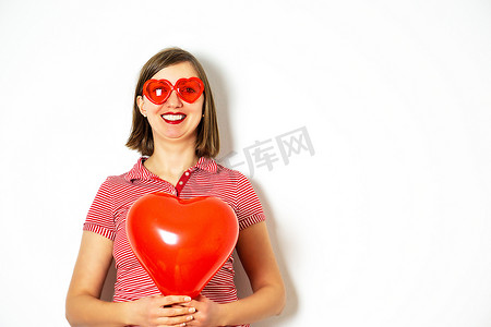 戴着红色太阳镜的美丽微笑女人手里拿着一个红色心形气球的画像。
